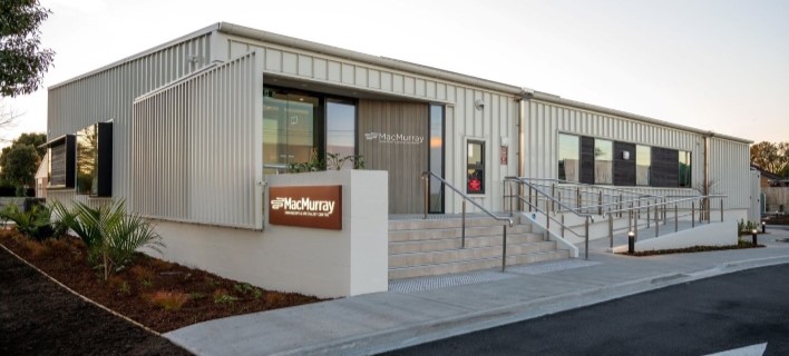 Modern medical facility with beige exterior, large windows, and MacMurray Centre sign, featuring accessible ramps.